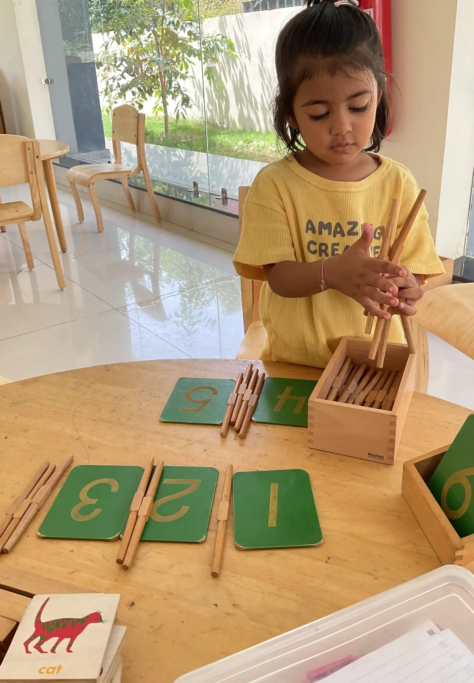 Child arranging wooden sticks and number cards on a table in a bright classroom