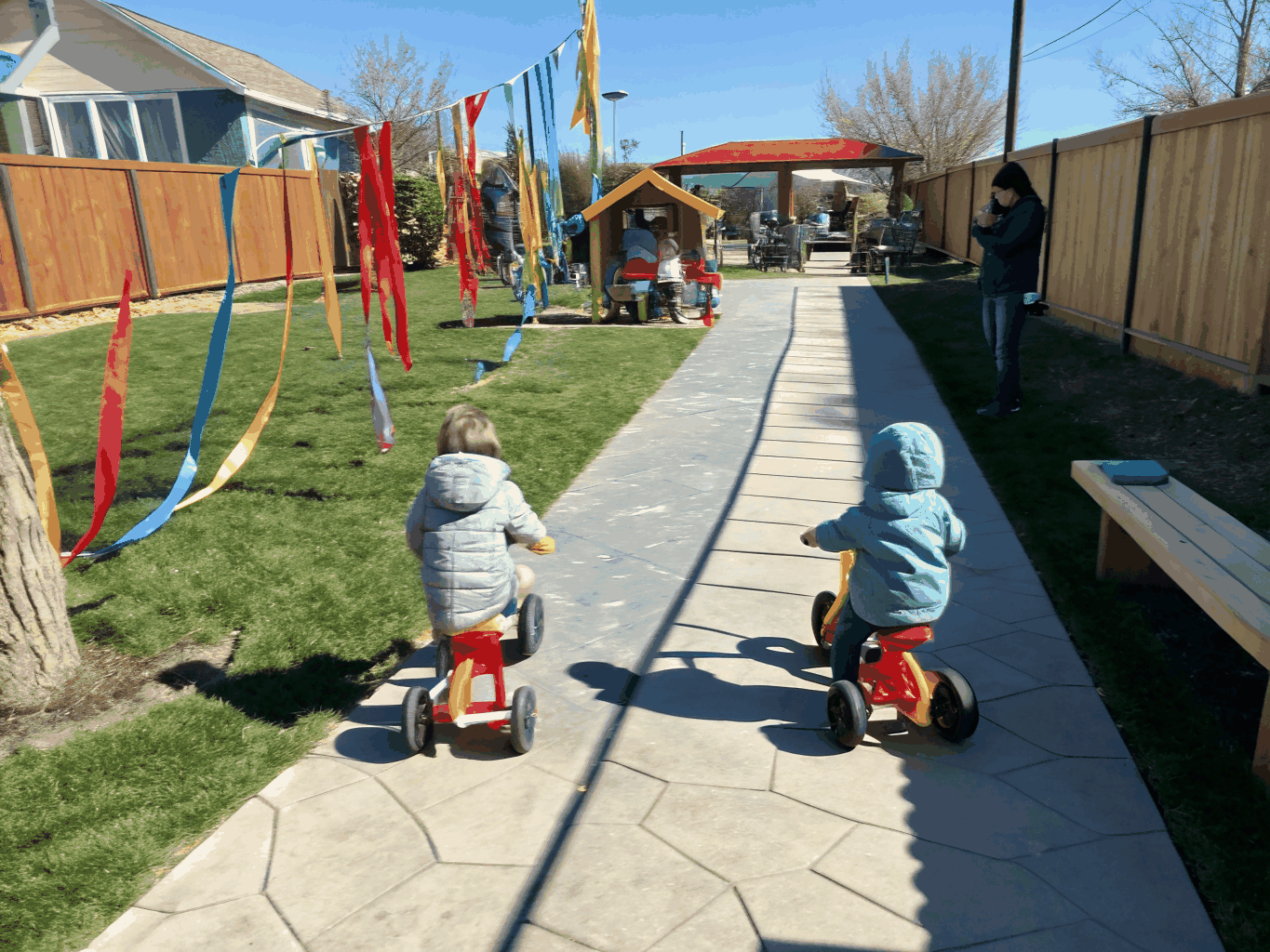 Toddlers navigating gently sloped timber obstacle and perimeter scooter path in morning light
