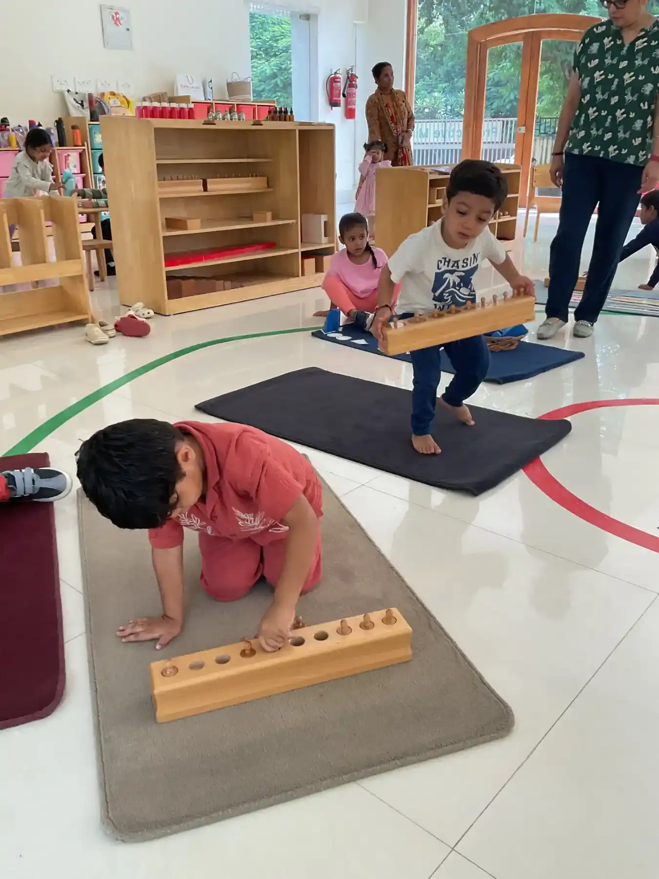 Toddler exploring Montessori sensorial cylinder blocks on a low wooden table in a sunlit classroom