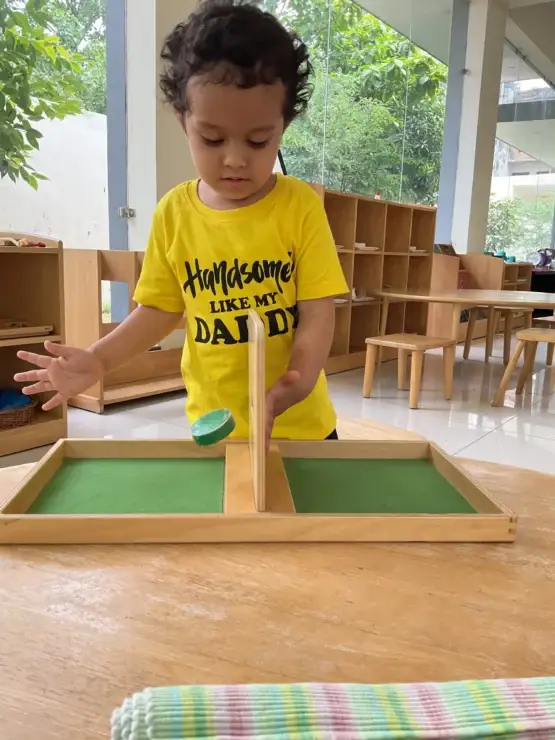 Toddler exploring Montessori sensorial cylinder blocks on a low wooden table in a sunlit classroom