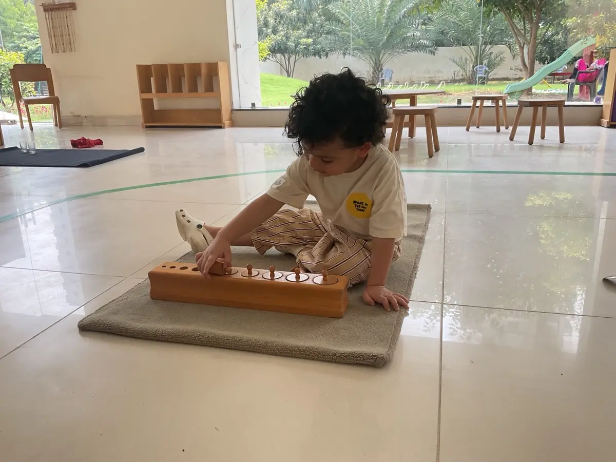 A toddler working with Montessori cylinder blocks